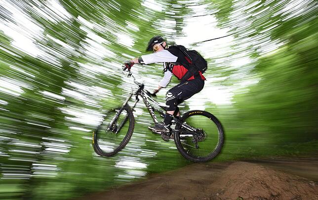 Ein Mountainbiker springt durch den Wald. Teilen sich Wanderer und Radler Strecken, kommt es ohne die nötige Rücksicht zu Konflikten.
