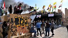 Demonstranten stehen mit Fahnen vor der Botschaft der Vereinigten Staaten in Bagdad, nachdem sie ein Feuer gelegt haben. Bild: dpa