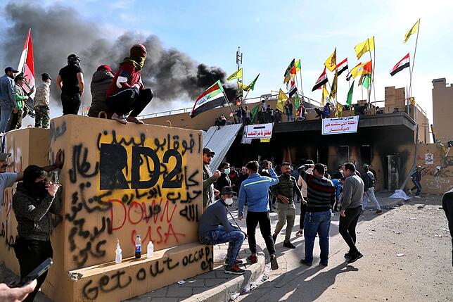Demonstranten stehen mit Fahnen vor der Botschaft der Vereinigten Staaten in Bagdad, nachdem sie ein Feuer gelegt haben. Bild: dpa
