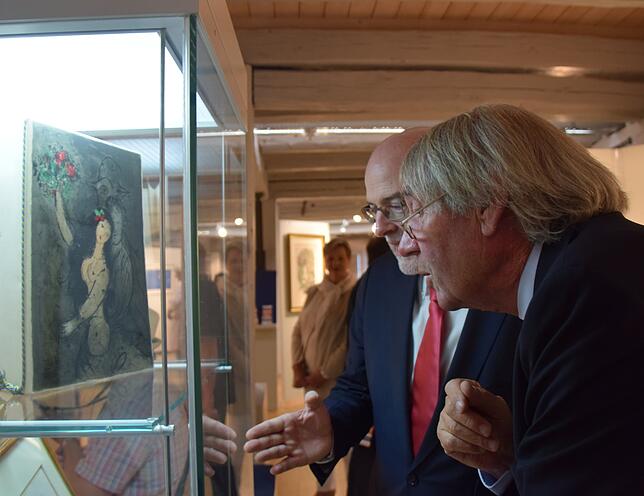 Chagall-Experte Roland Doschka (vorne) und Bürgermeister Rainer Stolz schauen sich ein Werk in einer Vitrine an.