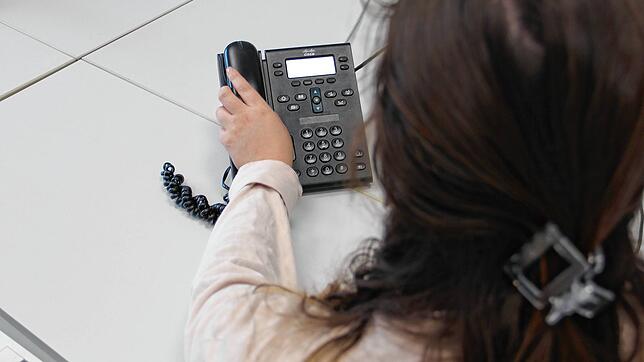 Eine Frau greift zum Telefonhörer. Immer wieder nutzen organisierte Banden das Telefon, um meist ältere Menschen dazu zu manipulieren, ...