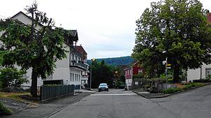 Die Burgfeldenstraße, rechts der Brunnen und die Dorflinde, vorne und hinten die Einmündungsarme der Lindenstraße. Parkende Autos, ...