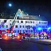 Der linke Teil des Mehrfamilienhauses hat ein ausgebranntes Dachgeschoss. Das Licht über dem Haus ist eine Drohne der Feuerwehr, die mit ...