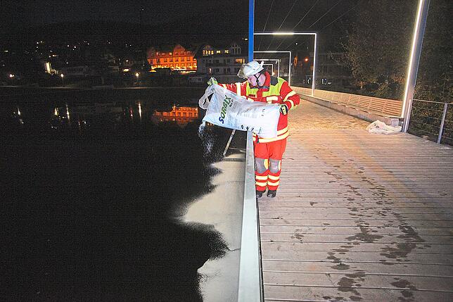 Von Land und von der Brücke aus streuen die Feuerwehrleute Bindemittel auf die Oberfläche des Eis- und Mühlenweihers.