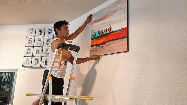 Mitarbeiter Nicolas Suarez Rivera bereitet den Kunstsupermarkt auf die Eröffnung vor, indem er Bilder an die Wand hängt.