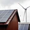 Hinter den Dächern eines Bauernhofes mit Photovoltaik produziert eine Windkraftanlage Öko-Strom. Diese Art Strom zu erzeugen ist nicht ...
