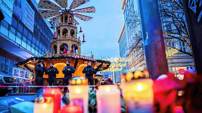 Polizisten sichern den Weihnachtsmarkt in Magdeburg. Im Vordergrund sind Kerzen zu sehen, die zum Gedenken an die Opfer der Todesfahrt ...