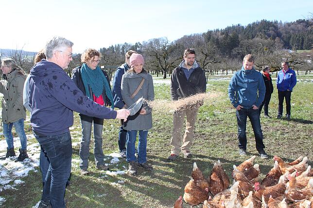Norbert Steidle (links) streut Futter aus und erklärt teilnehmenden Landwirten der "Lernort Bauernhof"-Exkursion, wie er seinen mobilen ...