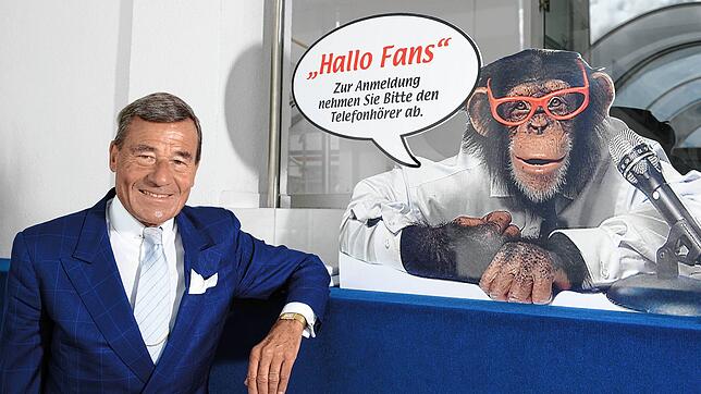 Wolfgang Grupp posiert am neben einem Werbeschild mit einem Affen.