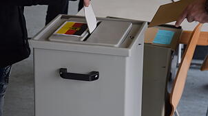 Ein Wähler wirft in der Herrischrieder Rotmooshalle einen Stimmzettel für die Bundestagswahl in eine mit der Bundesflagge markierten ...