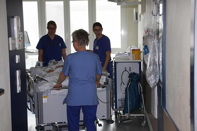 Einer der Intensiv-Patienten geht auf die Reise. Überwachungsgeräte, Sauerstoff und Unterlagen reisen auf dem Bett mit.