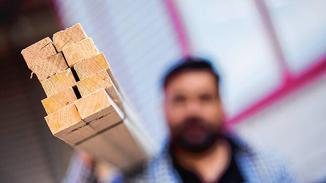 Ein Dachdeckermeister hält Dachlatten aus Holz. Um bis zu 90 Prozent haben sich Baustoffe 2021 verteuert.