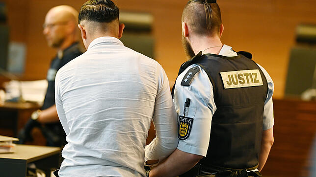 Einer von elf Angeklagten wird vor dem Prozessbeginn von einem Justizbeamten in den Gerichtssaal gebracht.