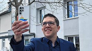 Dominik Männle steht mit seinem Handy und macht ein Selfie vor dem Rathaus in Uhldingen-Mühlhofen (gestelltes Bild). Für den ...