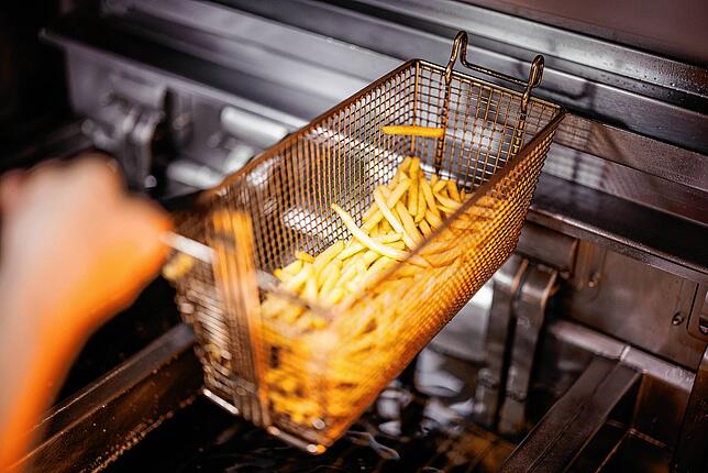 Eine Mitarbeiterin nimmt in einer Filiale der Fastfoodkette McDonald‘s einen Korb mit Pommes Frites aus der Friteuse. (Archivbild)