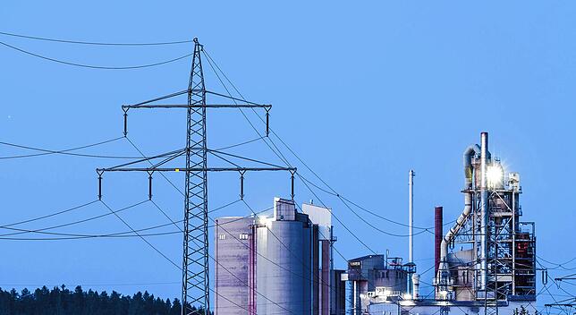 Strommasten stehen in Rottweil im Morgenlicht vor einem Zementwerk.