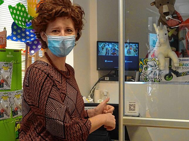 Anne Wilde steht neben dem QR-Code, der auf der Plexiglasscheibe an der Kasse hängt.