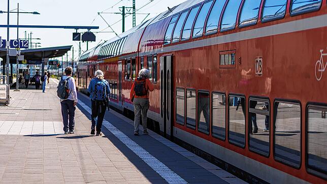 Reisende gehen neben einem Regionalexpress (RE) der Deutschen Bahn über den Bahnsteig.