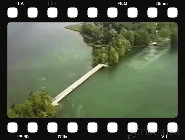 Filmstreifen Grünes Wasser und grüne Bäume: Die Brücke zur Blumeninsel Mainau (im Hintergrund) hebt sich hell ab von der Umgebung.