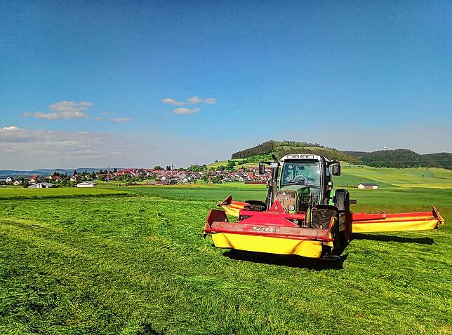 Ein Traktor mit ausgeklappten Mähwerken steht zwischen Behlaer Höhe und Fürstenberg.