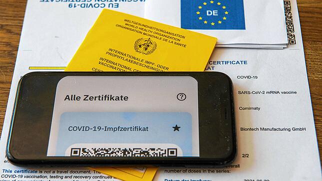 Ein Impfpass und ein Smartphone, auf dem die App CovPass läuft, liegen auf einem Impfzertifikat. (Symbolbild)