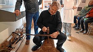 Fritz Wöhrle versucht sich während der Führung selbst und dengelt eine Sense.