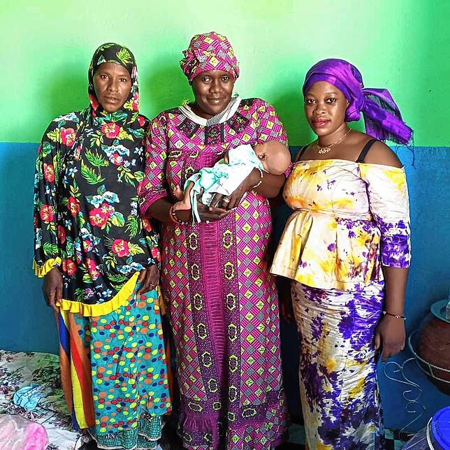Eine junge Mutter aus Mali (rechts) mit ihrem Neugeborenen, das in den Armen der Projektleiterin Fatumata liegt. Ganz links steht die ...
