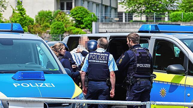 Der Mann wird von den Polizisten zu einem Streifenwagen eskortiert, er soll zur Vernehmung auf das Revier gebracht werden.