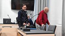 Der 84-jährige Angeklagte wird von einem Justizvollzugsbeamten zu seinem Platz begleitet.