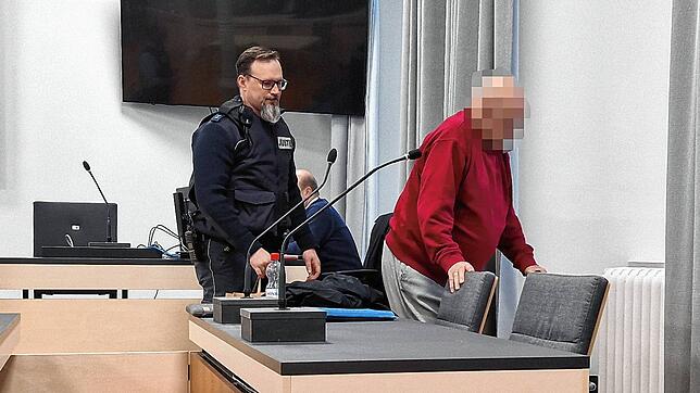Der 84-jährige Angeklagte wird von einem Justizvollzugsbeamten zu seinem Platz begleitet.
