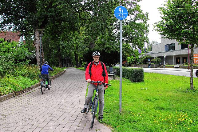 Steffen Lehr vom ADFC sitzt auf seinem Rad. Neben ihm steht ein blaues Verkehrsschild, welches einen gemeinsamen Geh- und Radweg am ...