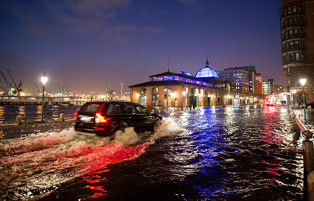 Ein Auto fährt 2017 in Hamburg während einer Sturmflut auf dem überfluteten Fischmarkt. Die Vorkehrungen gegen steigende Meeresspiegel ...