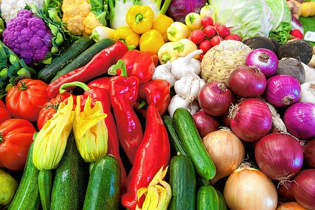 Hier liegen viele bunte Gemüsesorten, zum Beispiel Gurken, Tomaten und Paprika.