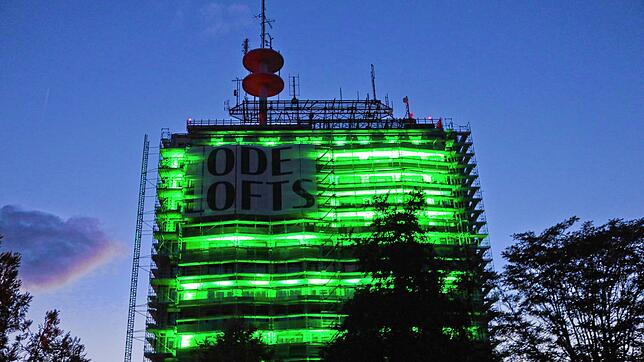 Der ehemalige Telekomturm in Petershausen leuchtet am Donnerstagabend, 8. August, grell und grün. Ein riesiges Werbebanner hängt am Gebäude.