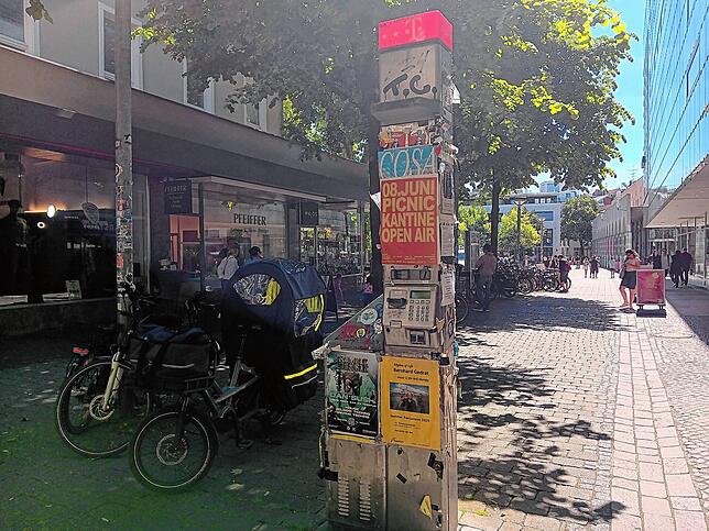 Eher Werbesäule als Telefonanlage: Zwischen einigen Fahrrädern auf dem Augustinerplatz steht eine von oben bis unten beklebte Telefonsäule.