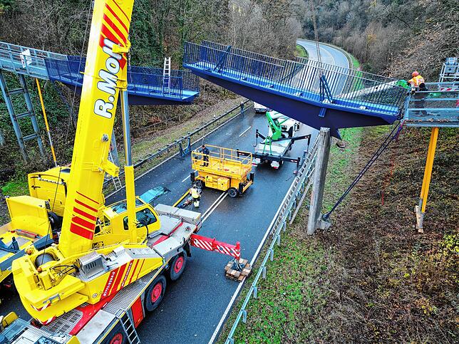 Nein, das ist keine Zugbrücke. Vielmehr hebt ein Schwerlastkran Teiler der Fußgängerbrücke bei Spetzgart in die Verankerung.
