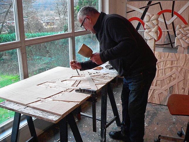 Josef Briechle bearbeitet mit Stechbeitel und Hammer eine Holzplatte.