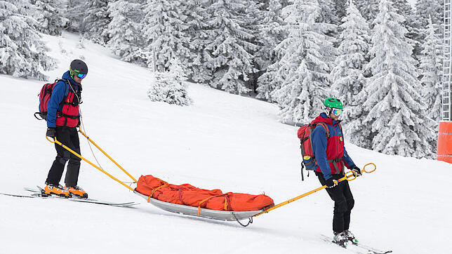 Ein Bergwacht-Mitglied auf dem Schneemobil unter einem landenden Hubschrauber (oben). Im Winter sind die Helfer bei ihren Einsätzen oft ...