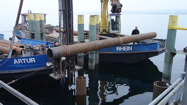 Der erste Teil der neuen Dalbe ragt schon aus dem Wasser. Das zweite Stück bringt der Bagger in die richtige Position, wo es dann ...