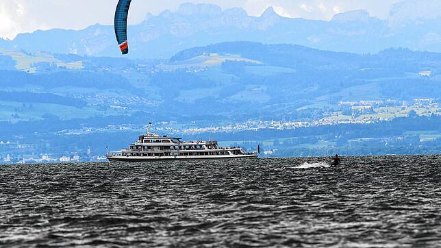 Ein Kitesurfer jagt an seinem Drachen bei Böen bis zu 40 Stundenkilometern über den Bodensee, während im Hintergrund ein Passagierschiff ...