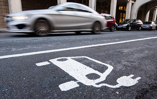 Ein Symbol eines Elektroautos markiert einen Parkplatz neben einer E-Ladesäule.