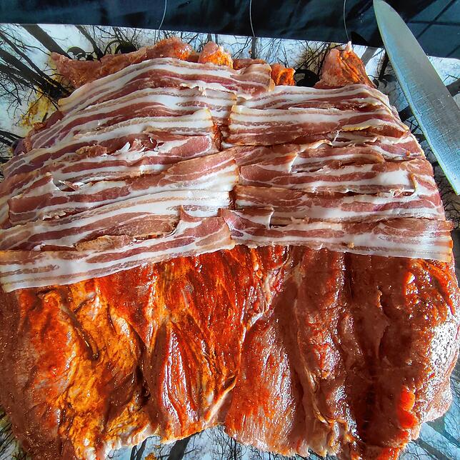 Die erste Lage im gewürzten Braten ist eine Lage mit hauchdünn geschnittenem Bauchspeck.
