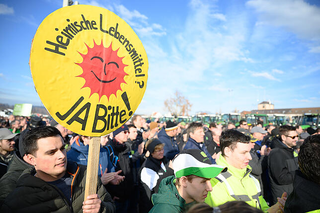 Ein Teilnehmer hält ein Schild mit der Aufschrift &ldquo;Heimische Lebensmittel? Ja Bitte!&bdquo;.
