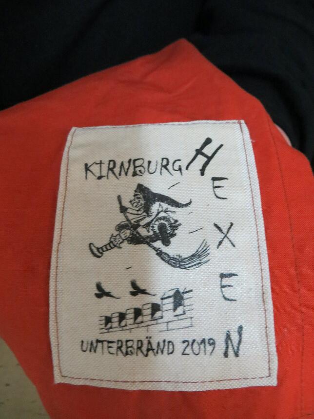 Eine wilde Hexe mit Besen: Das Logo der Kirnburghexen auf roten Schürze.
