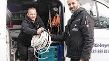 Sedat Tuncer (Anlagenmechaniker für Sanitär und Heizung) reicht Tolga Veron (Elektriker für Wärmepumpen und Photovoltaik) einen ...