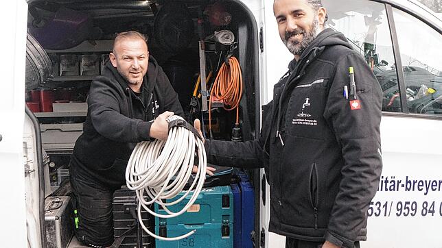Sedat Tuncer (Anlagenmechaniker für Sanitär und Heizung) reicht Tolga Veron (Elektriker für Wärmepumpen und Photovoltaik) einen ...