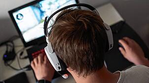 Ein Mann sitzt am mit einem Headset vor einem Laptop und spielt ein Online-Computerspiel.