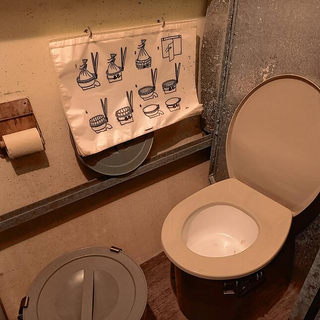 Blick in eine Trockentoilette mit der Gebrauchsanleitung für die Plastiksack, der hier einzusetzen und zu verschließen ist.