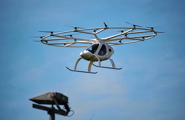 Ein Volocopter fliegt vor blauem Himmel. Das elektrisch angetriebene Vehikel, das aussieht wie eine Mischung aus Hubschrauber und ...
