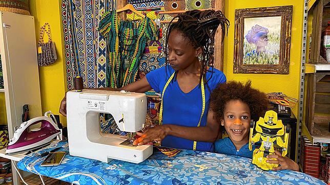 Philadelphia Shayi steht mit dem Bügelbrett und der Nähmaschine im Erlebnisatelier &bdquo;eKhaya&ldquo;. Sie näht ihre Masken aus ...